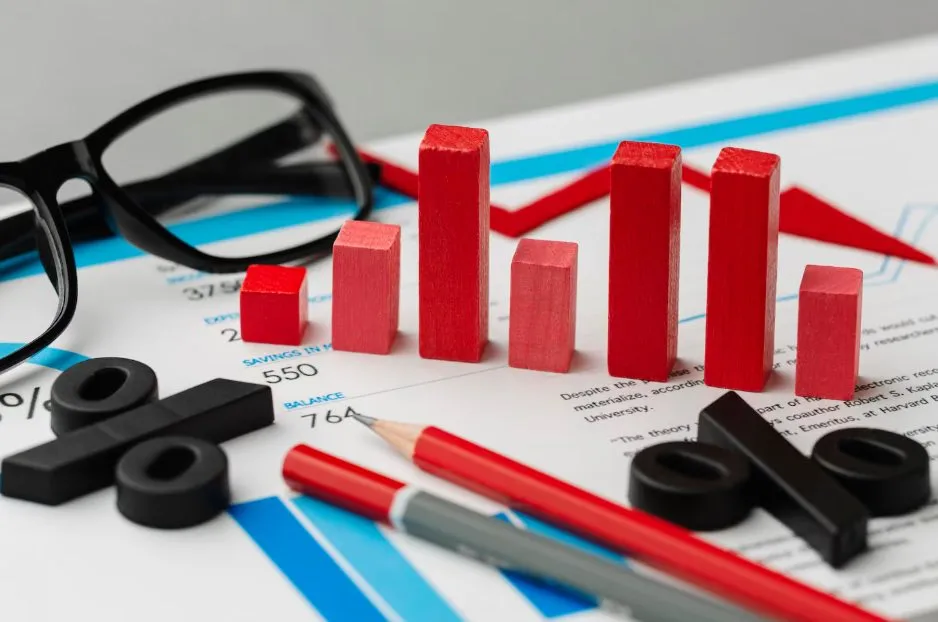 Red wooden blocks arranged as a bar chart on a printed report beside glasses and a pencil