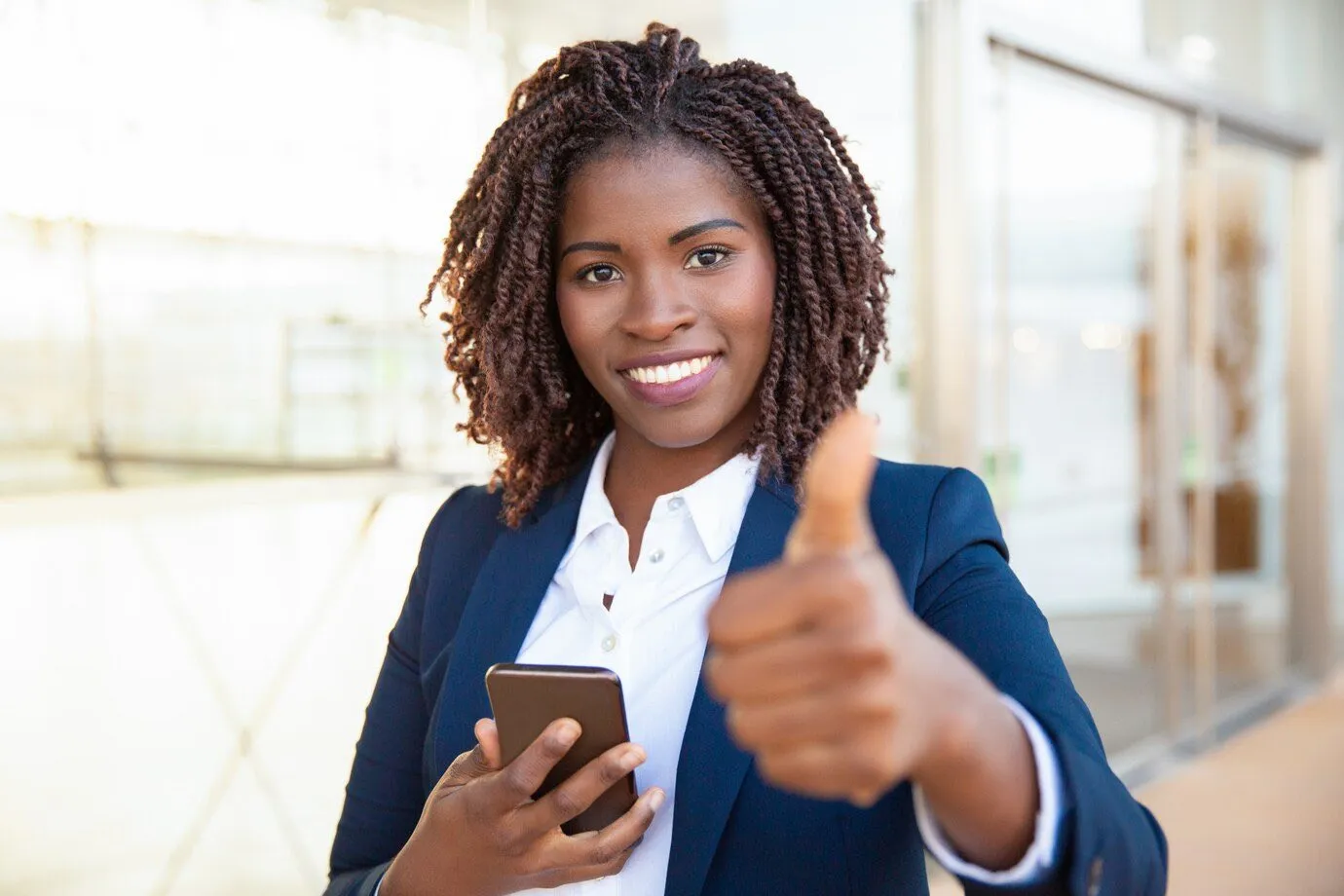 A businesswoman holding a phone and giving a thumbs up