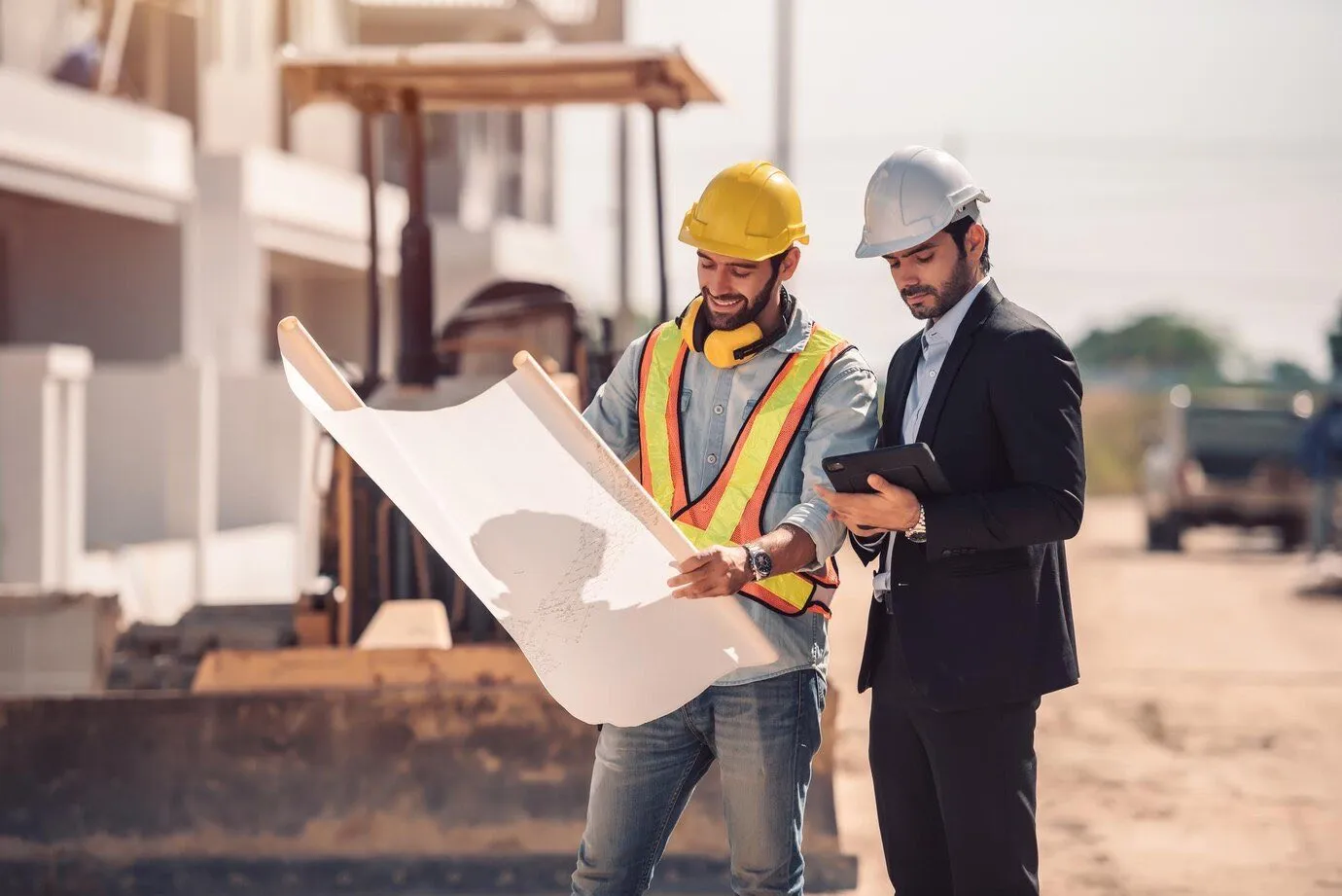 A contractor in a hard hat and an architect reviewing building plans on a construction site