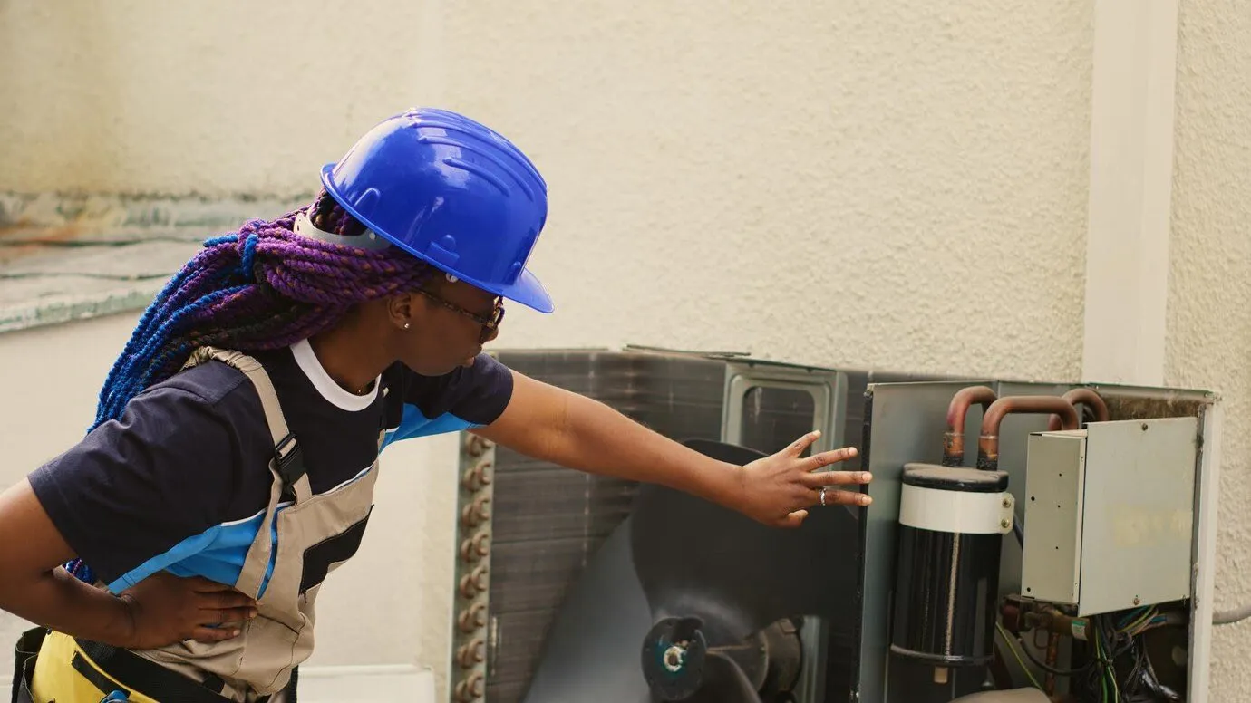 An engineer in a hard hat servicing an outdoor air conditioning unit