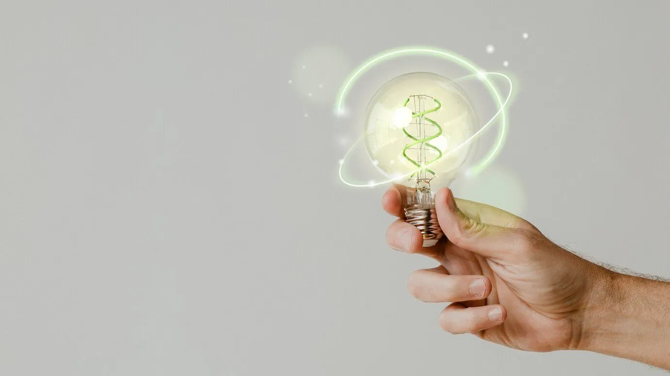 A hand holding a glowing lightbulb encircled by a ring of green light