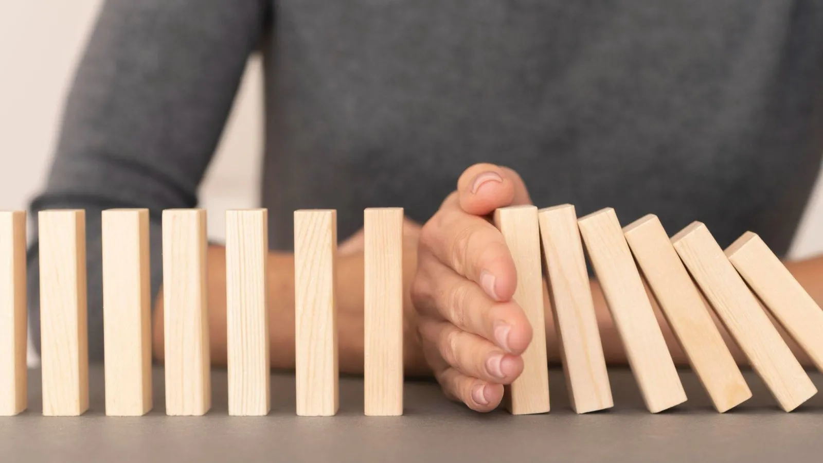 A hand stopping a line of falling wooden dominoes