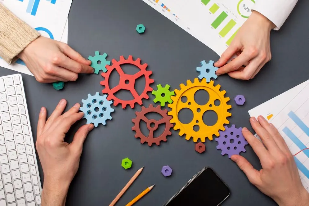 Hands arranging interlocking coloured cogs on a desk