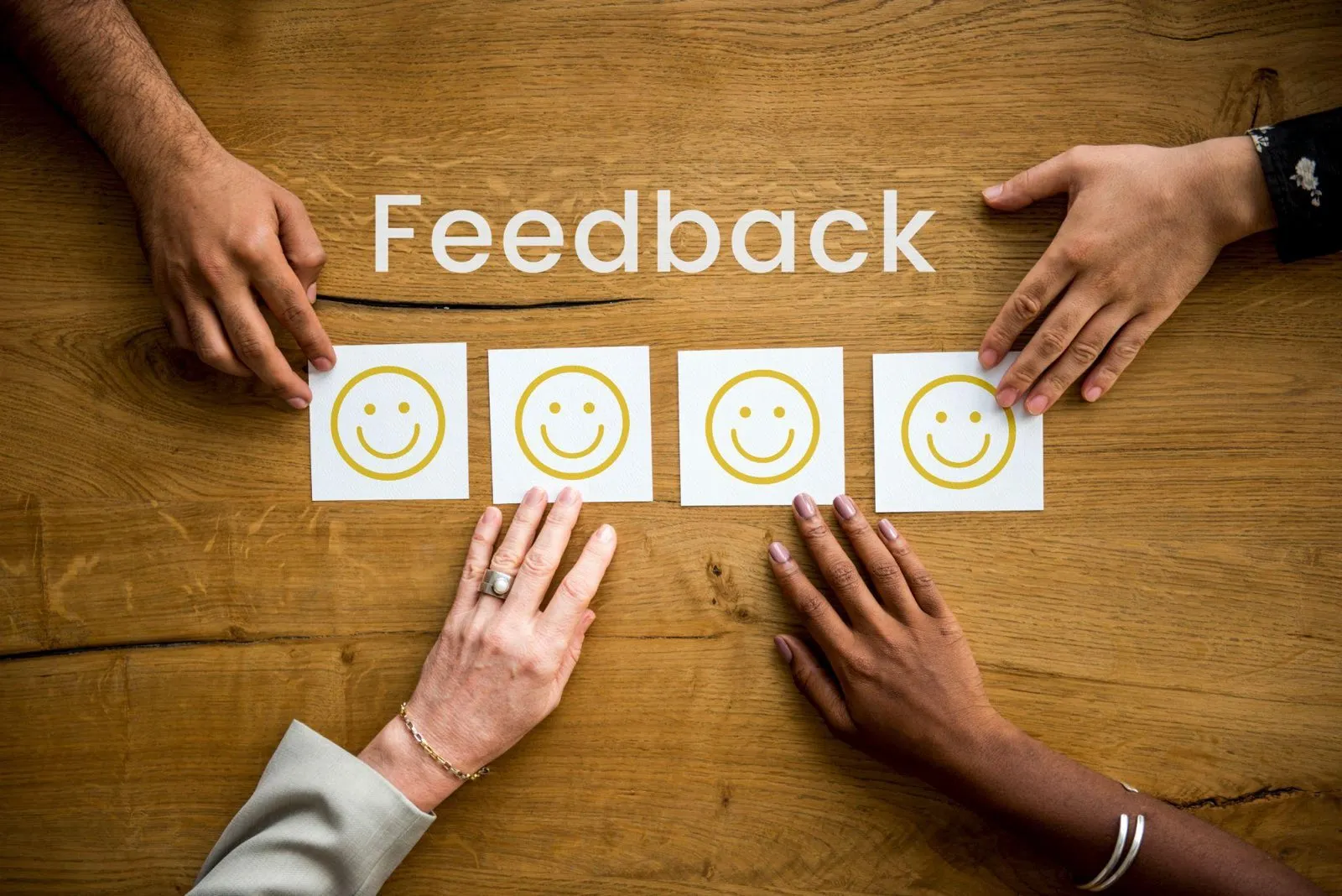 Four pairs of hands arranging cards showing smiling faces under the word Feedback