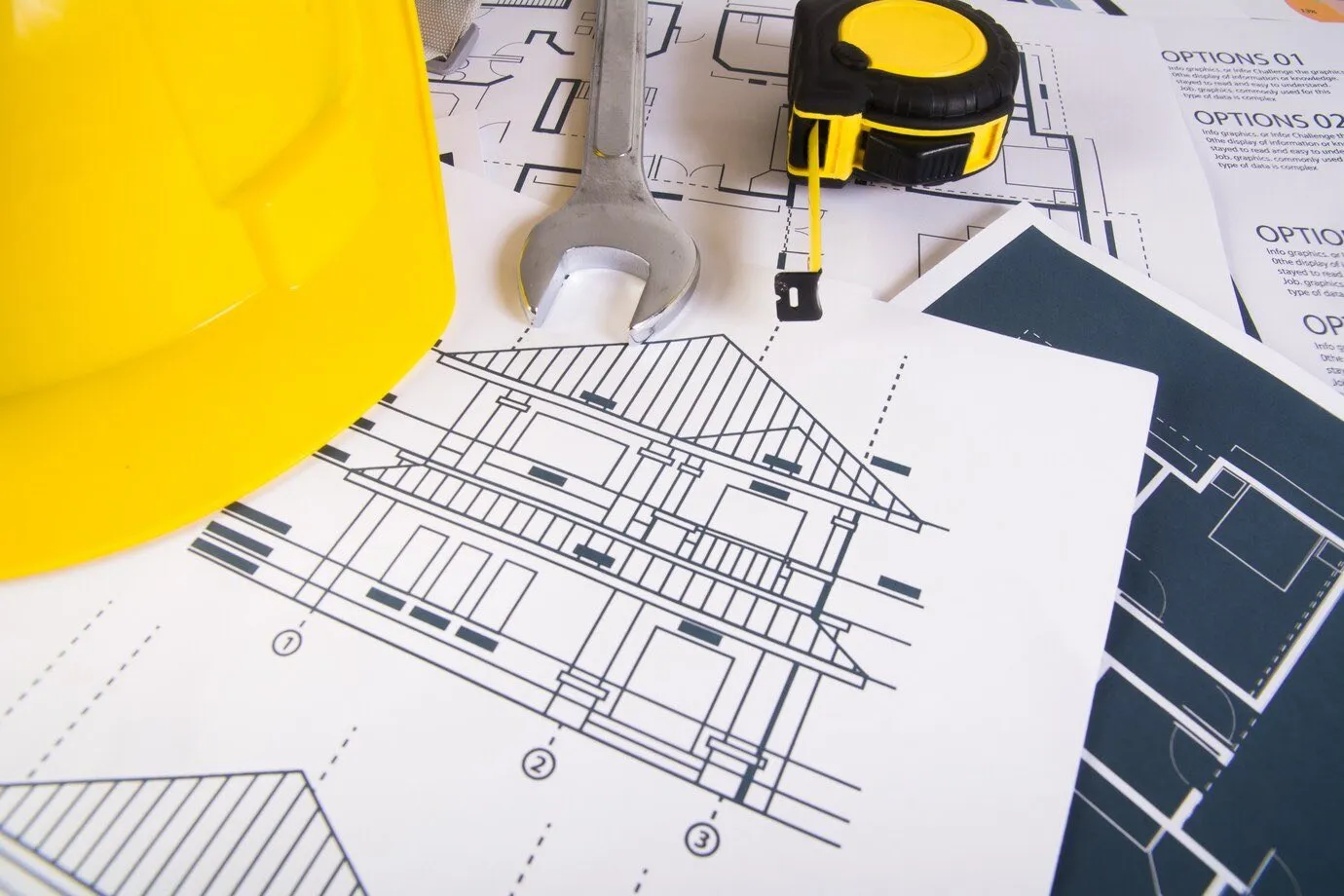 A yellow hard hat and tape measure resting on printed building plans