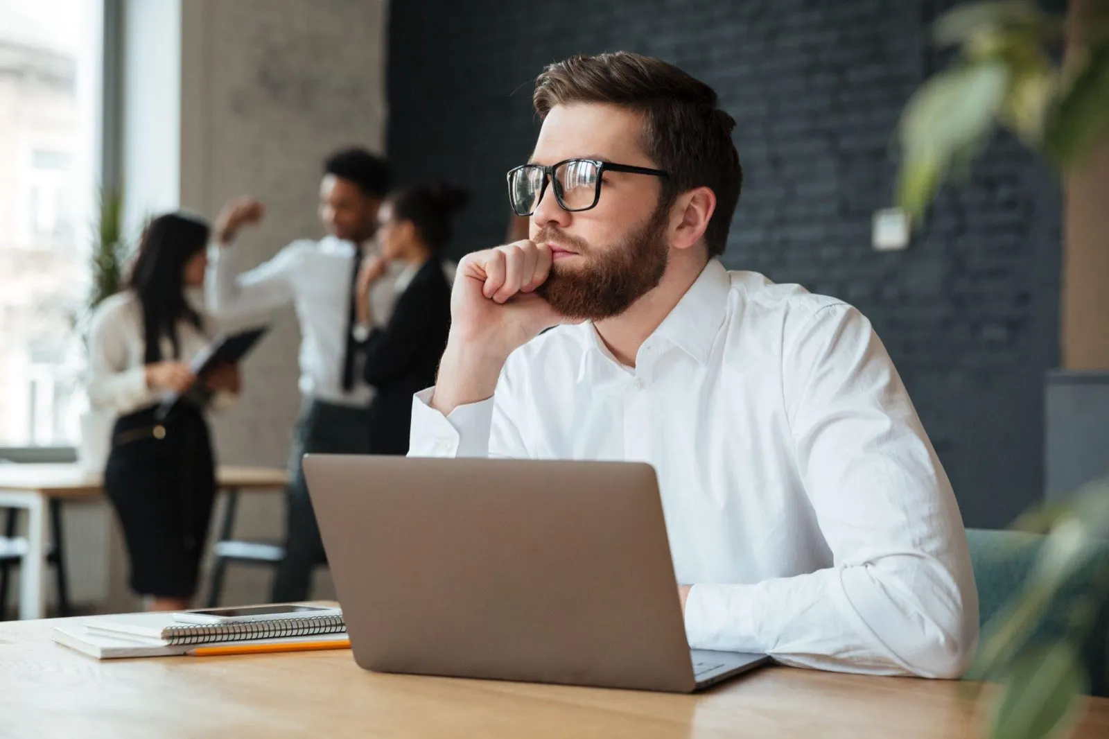 A manager sitting at a laptop in an open-plan office, deep in thought