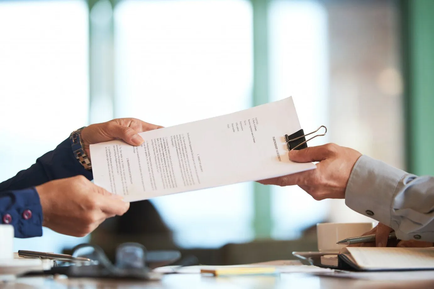 Two people passing a printed document across a desk