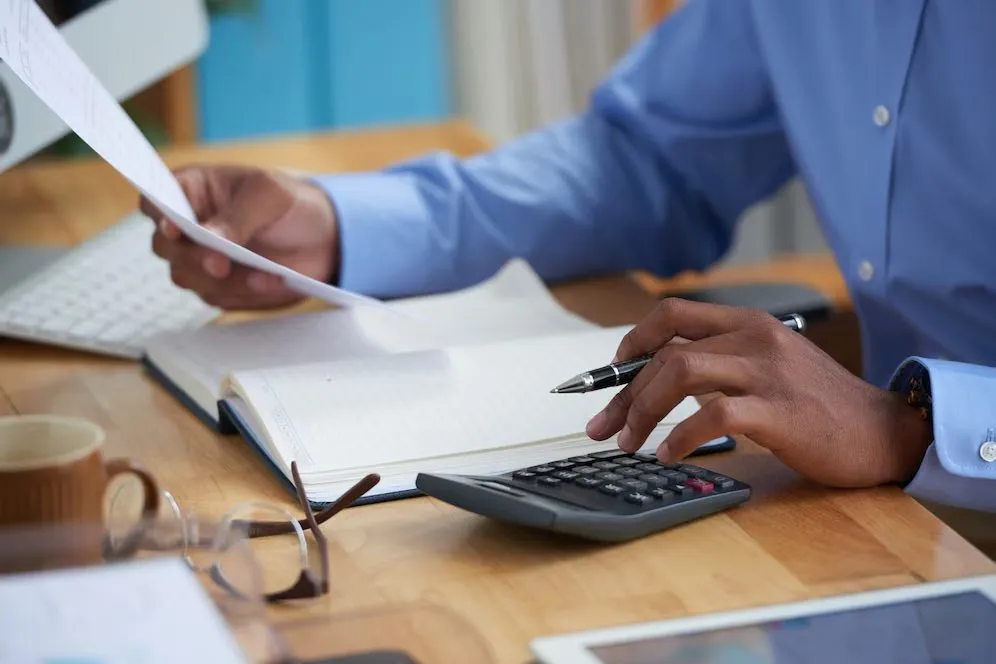 A person reviewing printed paperwork while using a calculator