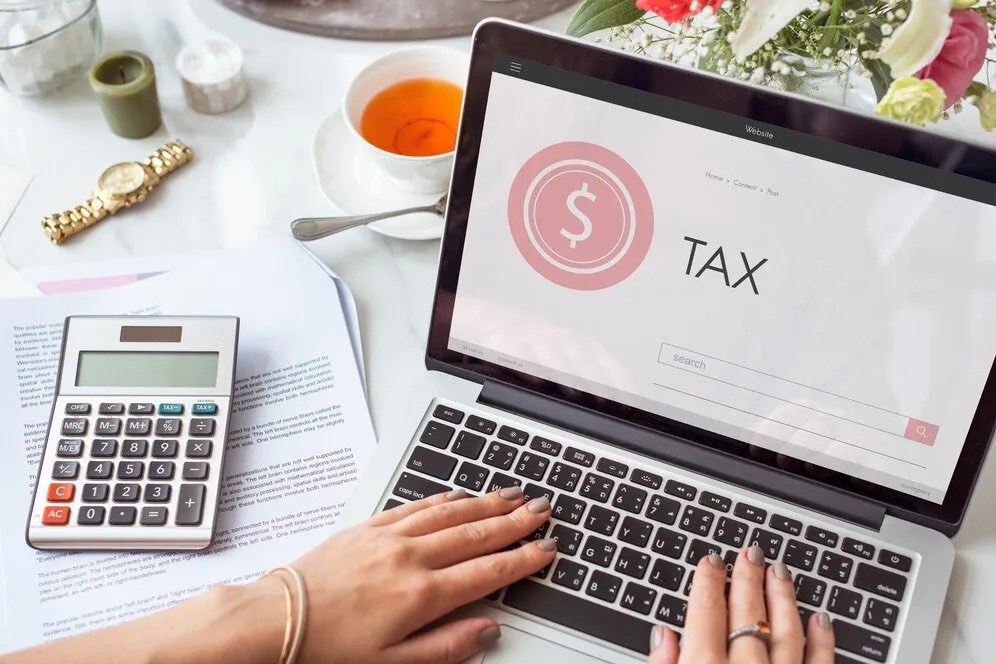 A laptop showing a tax page beside a calculator and paperwork
