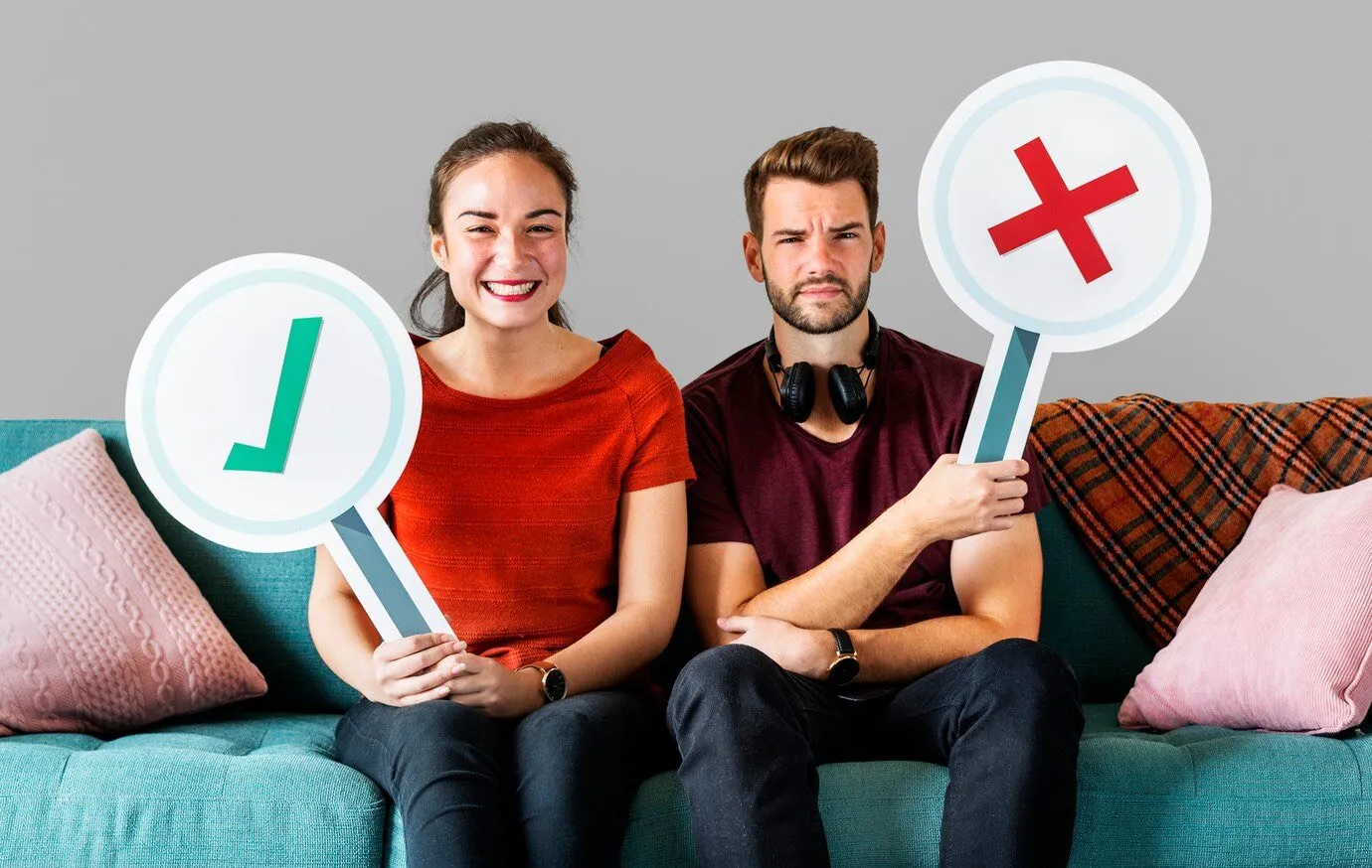 Two people on a sofa holding up a green tick and a red cross