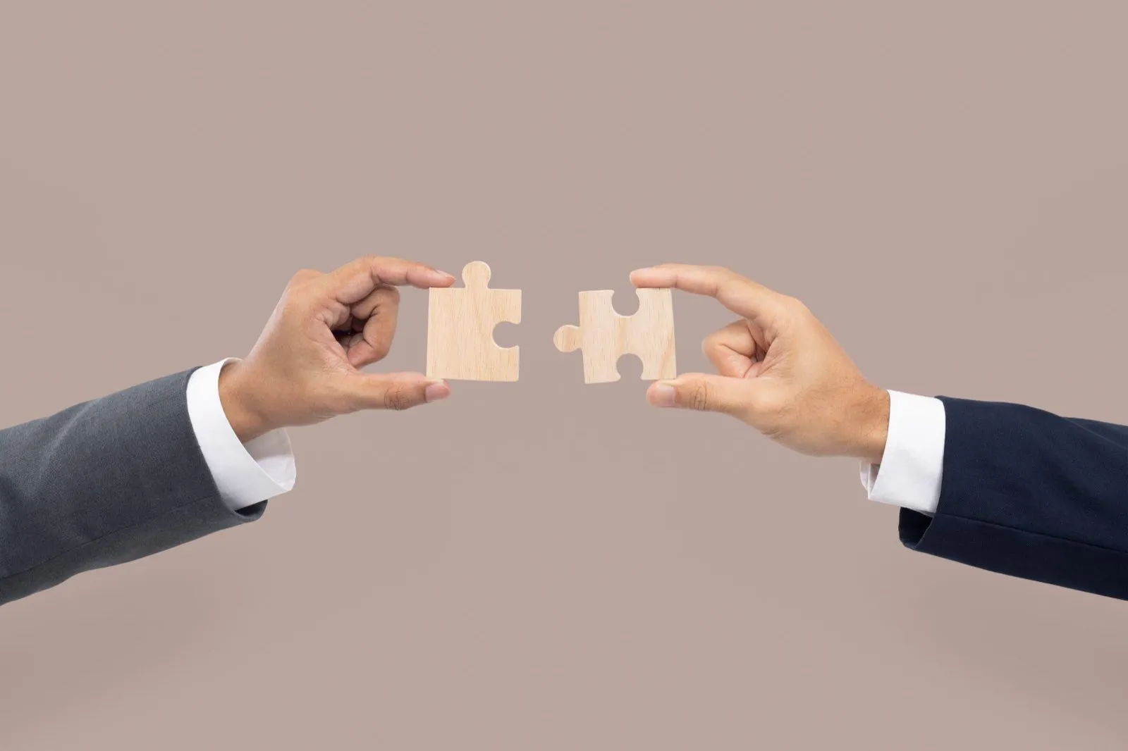 Two people in suits fitting two jigsaw pieces together