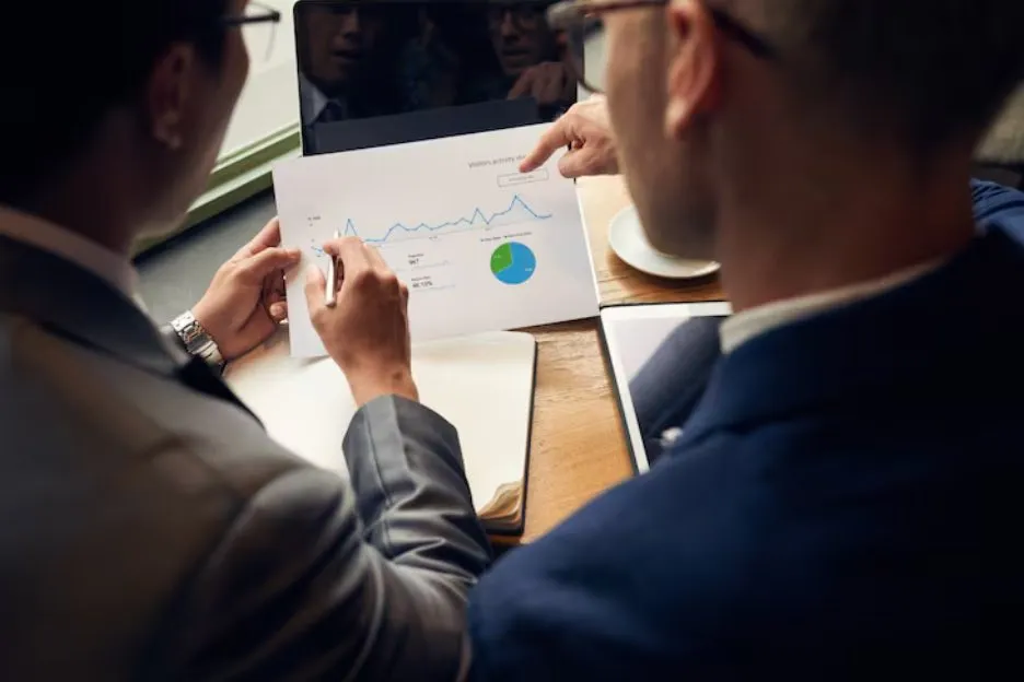 Two people in a meeting reviewing a printed chart of performance data