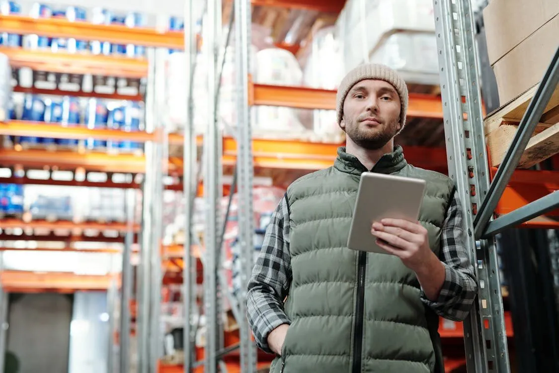A warehouse worker checking stock on a tablet beside racked shelving