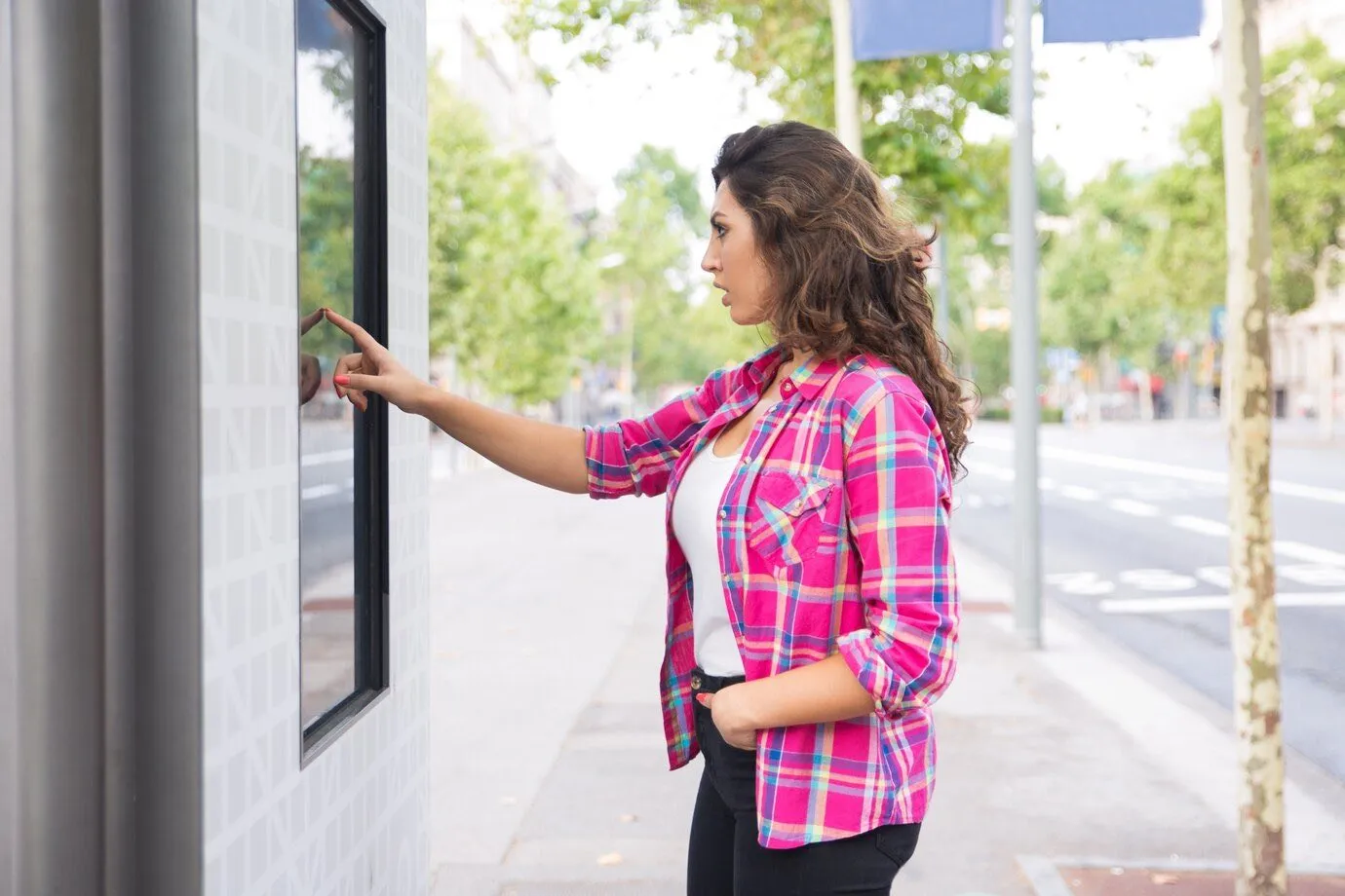 A woman using a touchscreen self-service kiosk on a street
